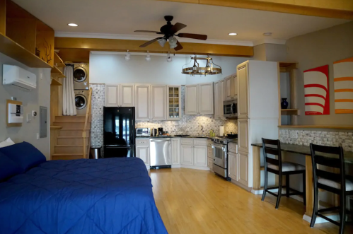 Cozy studio apartment with a bed, kitchen, dining area, and laundry, featuring modern decor and wooden accents.