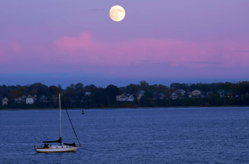 A serene scene of a sailboat on water under a large full moon and a colorful twilight sky.