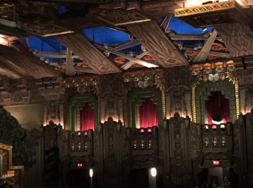 Interior of a theater featuring ornate architecture, red curtains, and a decorative ceiling with intricate designs.