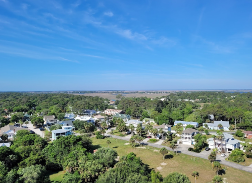 Aerial view of a coastal town with greenery, houses, and a blue sky in the background.