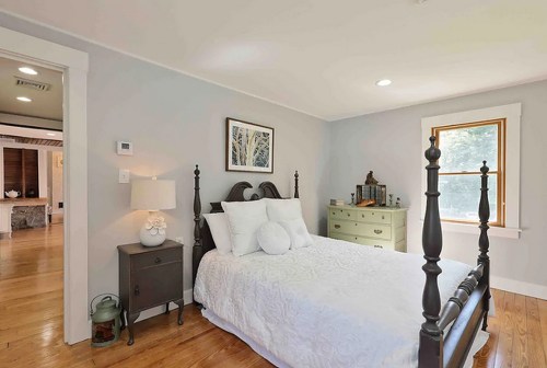 Cozy bedroom with a black bed frame, white bedding, a nightstand, and a window letting in natural light.