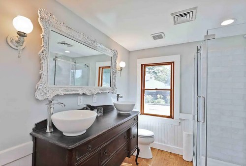 Bright bathroom featuring a vintage mirror, modern sink, and a glass shower, with natural light from a window.