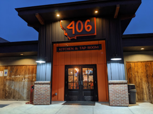 Exterior of 406 Kitchen & Tap Room, featuring a dark facade, orange accents, and a welcoming entrance at dusk.