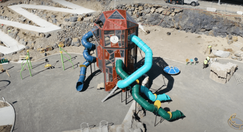 A colorful playground structure with multiple slides and climbing features, set in a rocky outdoor area.