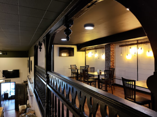 A cozy restaurant interior featuring wooden tables, chairs, and warm lighting, viewed from a balcony.