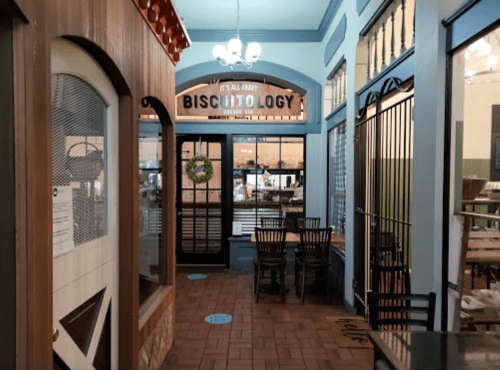 Interior view of a cozy hallway leading to a restaurant called "Biscuitology," featuring wooden furniture and decorative elements.