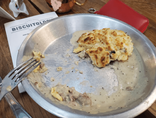 A partially eaten plate of biscuits and gravy, with a fork resting beside it, and a menu in the background.