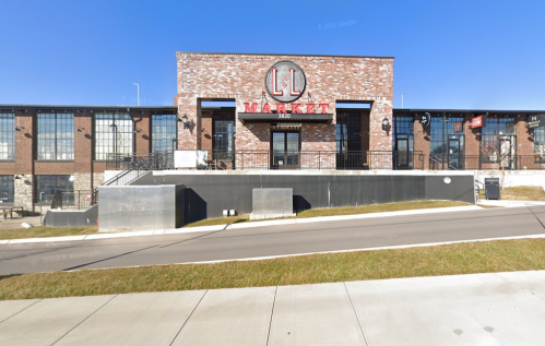 Exterior view of LL Market, a brick building with large windows and a prominent sign, set against a clear blue sky.