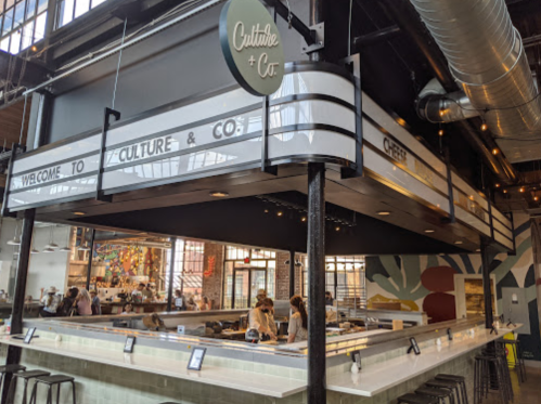 Interior of a modern restaurant with a welcoming sign, open kitchen, and vibrant decor.