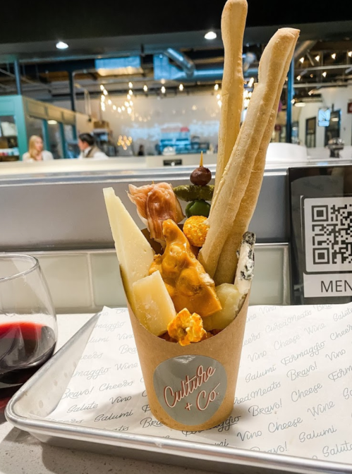 A cup filled with assorted cheeses, popcorn, breadsticks, and a decorative figure, set in a cozy dining space.