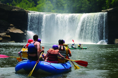 A group of people in colorful rafts paddling near a waterfall, surrounded by lush greenery.