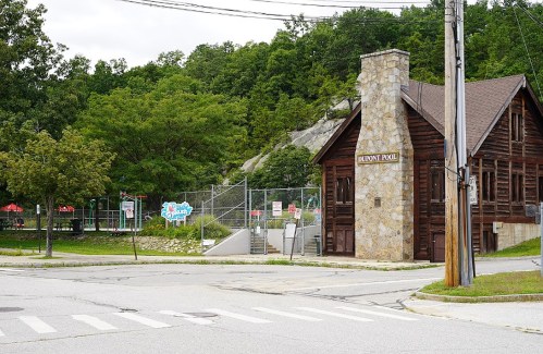 A rustic stone building labeled "Dupont Pool" near a fenced pool area, surrounded by trees and a street.