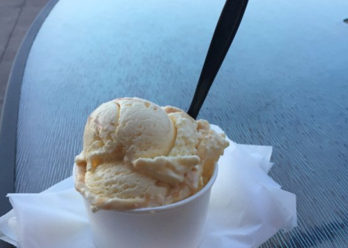 A cup of creamy ice cream with a black spoon, resting on a napkin beside a reflective surface.