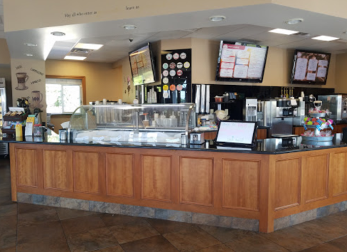 A bright café interior featuring a service counter with a glass display, menus on screens, and colorful decor.