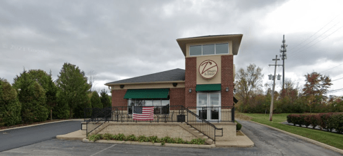 A brick building with a green awning, featuring an American flag, surrounded by trees and a cloudy sky.