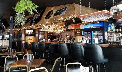 A cozy bar interior with black stools, a well-stocked back bar, and festive decorations.