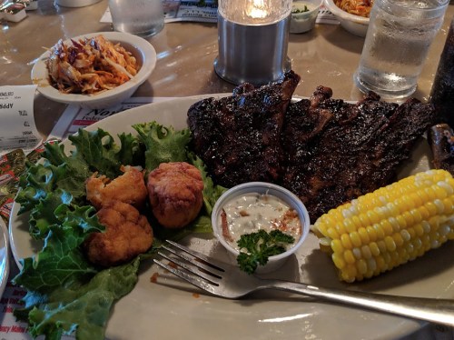 A plate of grilled ribs with corn, fried chicken, lettuce, and dipping sauce, served at a restaurant.