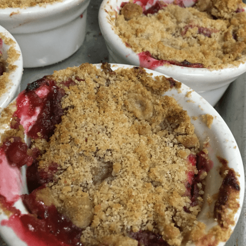 Close-up of individual fruit crumbles in white ramekins, topped with a golden brown crumbly topping.