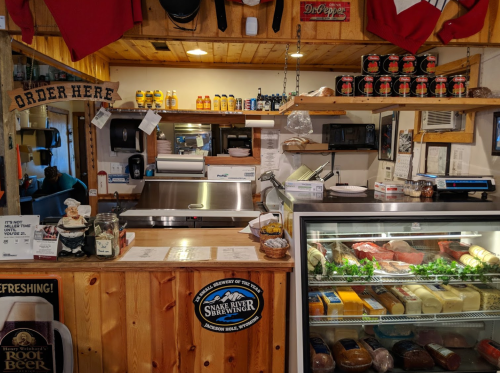 A rustic counter at a deli with a meat display, condiments, and a sign that says "Order Here."