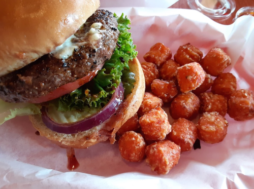 A juicy hamburger with lettuce, tomato, and onion, served with a side of crispy tater tots.