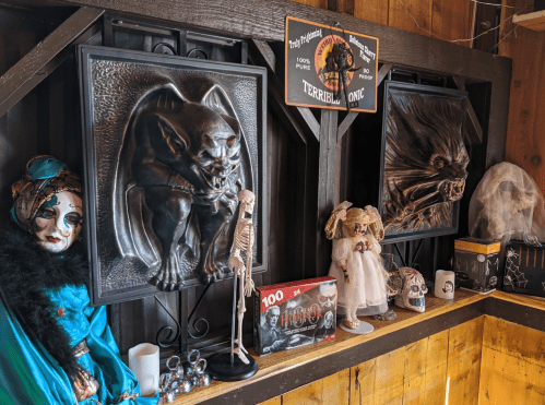 A display featuring eerie decorations, including framed monster art, dolls, and Halloween-themed items on a wooden shelf.