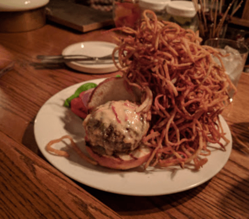 A plate with a burger topped with sauce and lettuce, accompanied by a large pile of crispy fried onions.