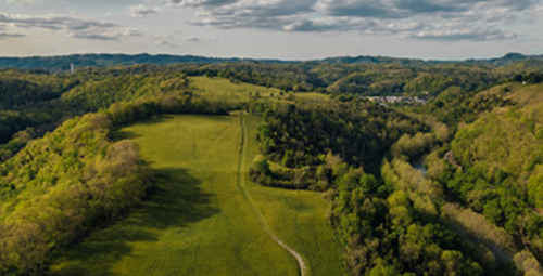 Aerial view of lush green hills and valleys under a partly cloudy sky, with a winding path through the landscape.