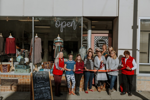 A group of people holding a ribbon in front of a store with an "open" sign, celebrating a grand opening.