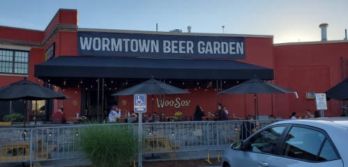 Exterior of Wormtown Beer Garden with outdoor seating and umbrellas, people enjoying drinks in a lively atmosphere.