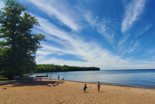 A sunny beach scene with people relaxing, children playing, and a clear blue sky over calm water.