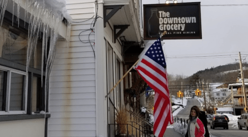 A woman walks past The Downtown Grocery, featuring an American flag and icicles hanging from the building.