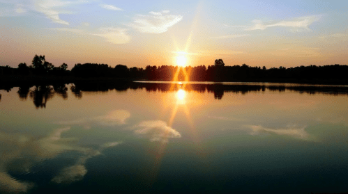 A serene sunset over a calm lake, with reflections of the sky and trees in the water.