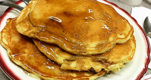 A stack of fluffy pancakes drizzled with syrup on a white plate.