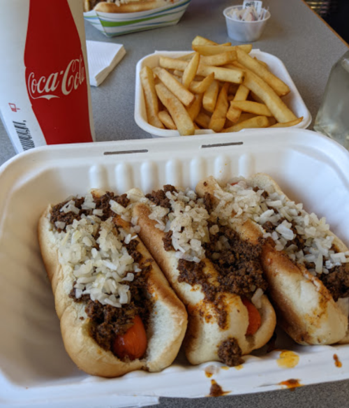 Three hot dogs topped with chili and onions, served with a side of French fries and a Coca-Cola.