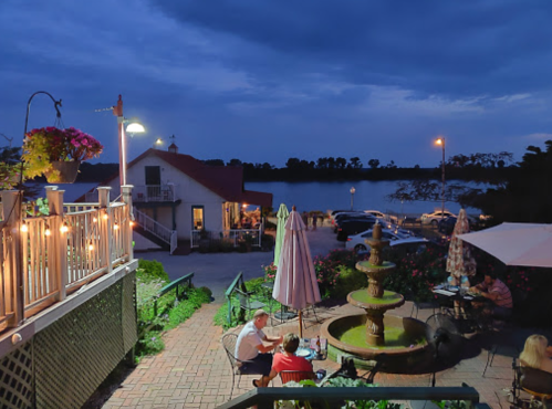 A serene evening scene by a waterfront restaurant, featuring a fountain, outdoor seating, and soft lighting.