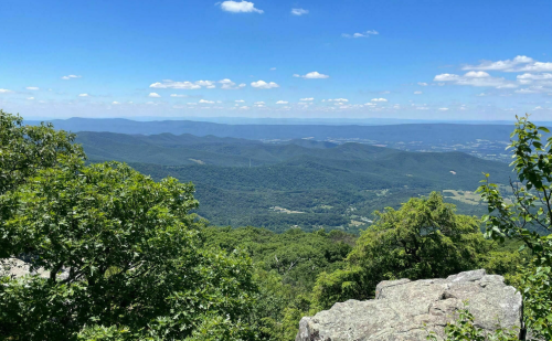 A panoramic view of lush green mountains under a bright blue sky with scattered clouds.