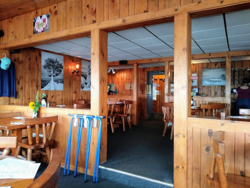 Cozy wooden interior of a restaurant with tables, photos on the walls, and blue walking poles by the entrance.