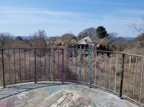 View from a balcony overlooking a desolate landscape with a ruined building and the ocean in the distance.