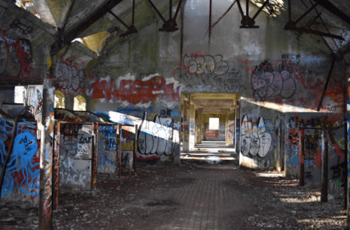 Abandoned building interior with graffiti-covered walls and sunlight streaming through broken windows.