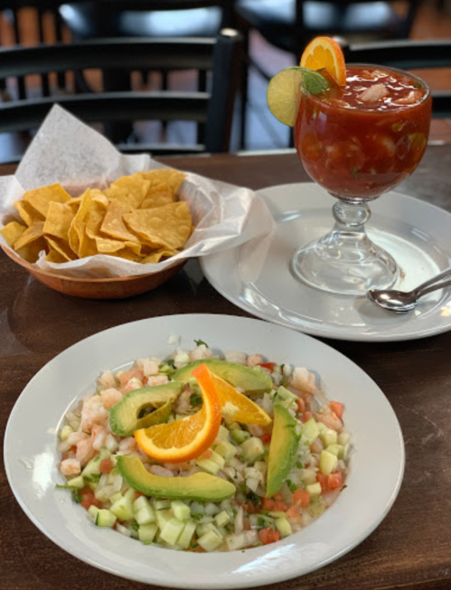 A plate of shrimp ceviche with avocado and orange slices, accompanied by tortilla chips and a glass of cocktail.