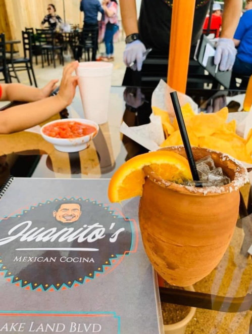 A table at a Mexican restaurant featuring a menu, a drink with an orange slice, chips, and salsa.