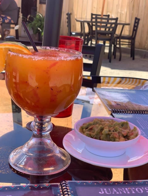 A vibrant orange cocktail with a slice of orange and a side of guacamole on a table at a restaurant.