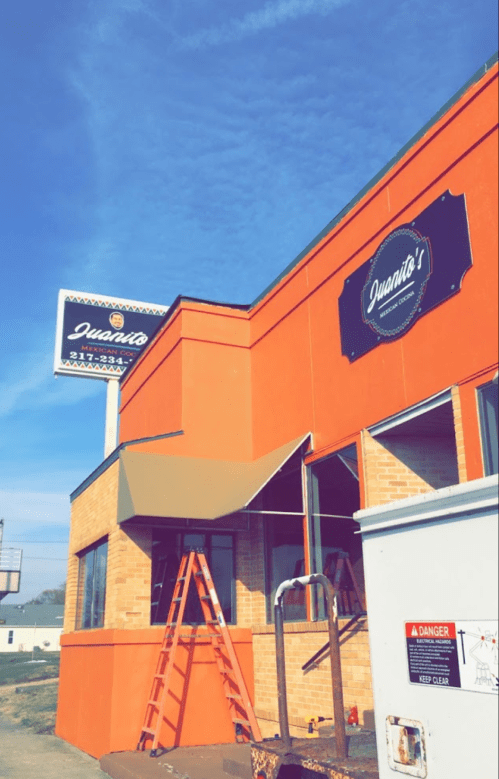Exterior of Juanito's restaurant with a ladder, orange brick wall, and clear blue sky.