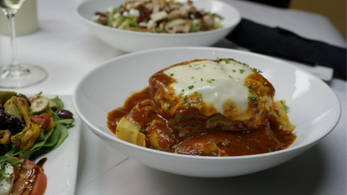 A plate of lasagna topped with melted cheese and marinara sauce, served with a side salad.