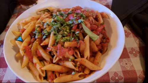 A bowl of penne pasta topped with fresh basil and a rich tomato sauce, served on a checkered tablecloth.