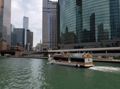 A boat navigates the Chicago River, surrounded by tall buildings and reflections on the water.
