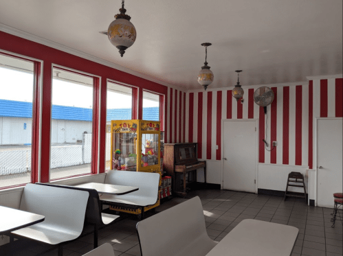 Interior of a diner with red and white striped walls, tables, vintage lamps, a jukebox, and a toy vending machine.