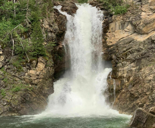 A powerful waterfall cascading down rocky cliffs into a serene pool below, surrounded by lush greenery.