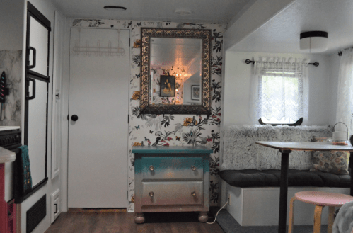 Cozy interior of a trailer with floral wallpaper, a mirror, a colorful dresser, and a seating area.