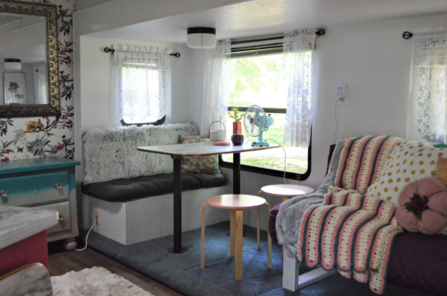 Cozy interior of a trailer with a dining area, plush seating, and bright natural light from large windows.